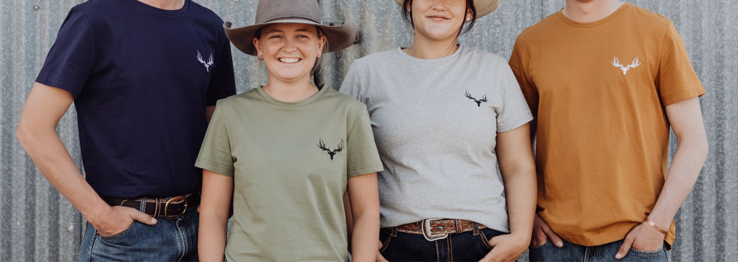 Two men and two women stand in front of a shed wearing Rawhide Rural staple tees