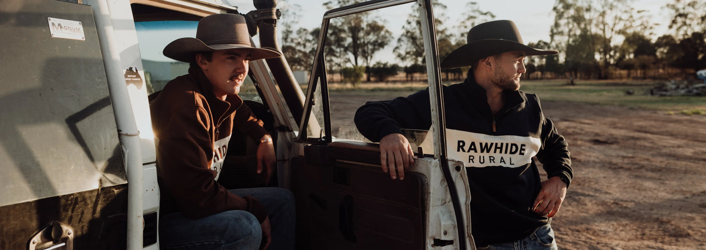 Two men standing next to the door of a Toyota Landcruiser wearing Rawhide Rural quarter zip jumpers