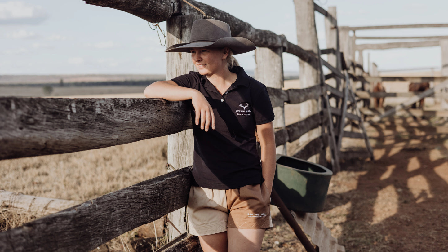 Person wearing a navy shirt and hat leaning against a wooden fence on a farm.