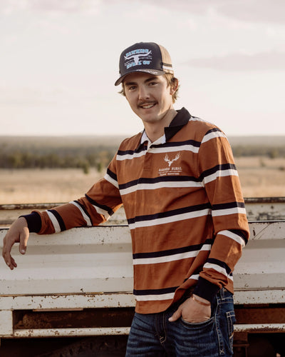 Man standing next to a ute in an open field wearing a rugby jumper