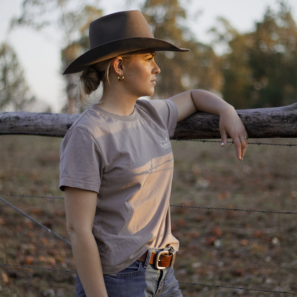 
                  
                    Woman wearing a hat and casual outfit leaning against a fence with a natural background
                  
                
