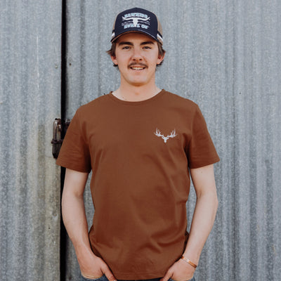 A man standing in front of grey background wearing a brown shirt.