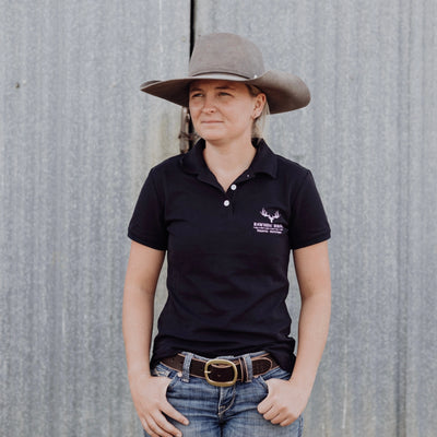 Woman wearing navy polo shirt against grey background.