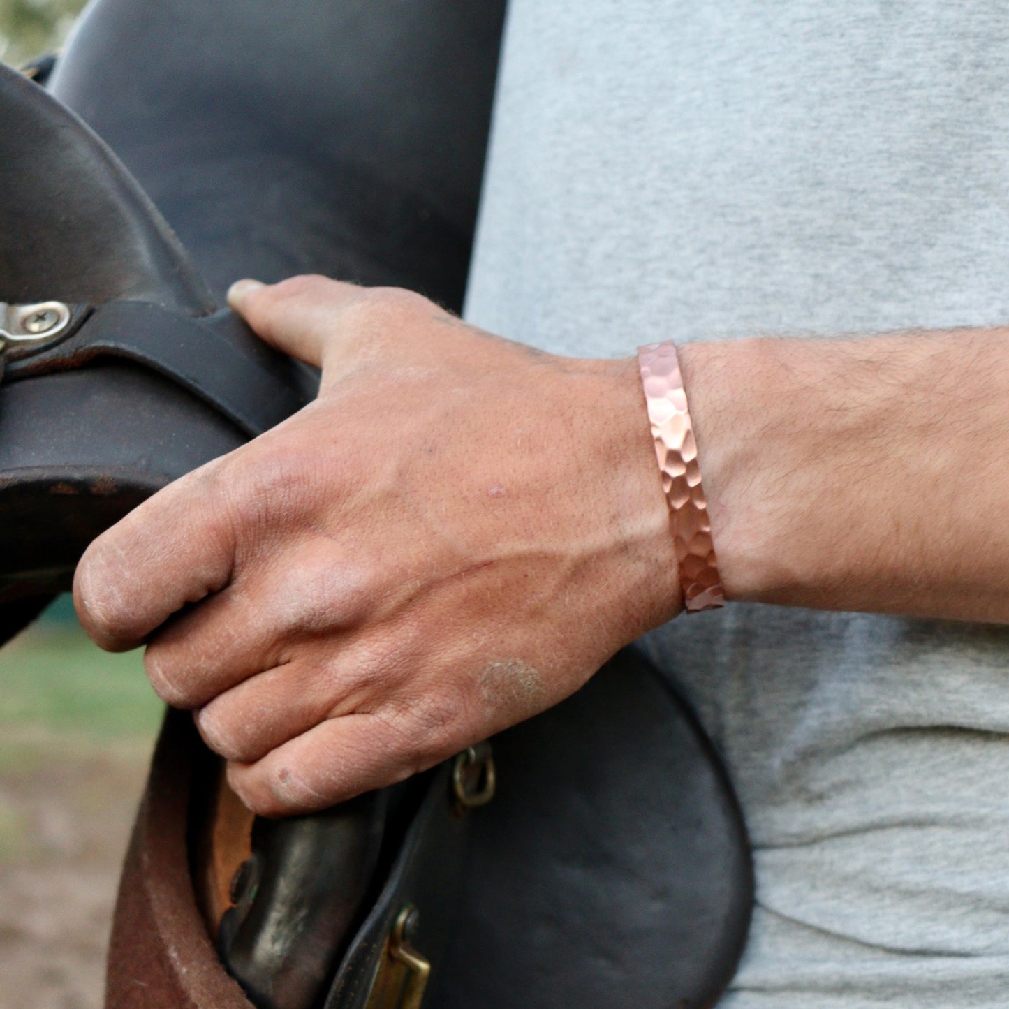 Hand holding a leather saddle with a person wearing a beaten copper bracelet.
