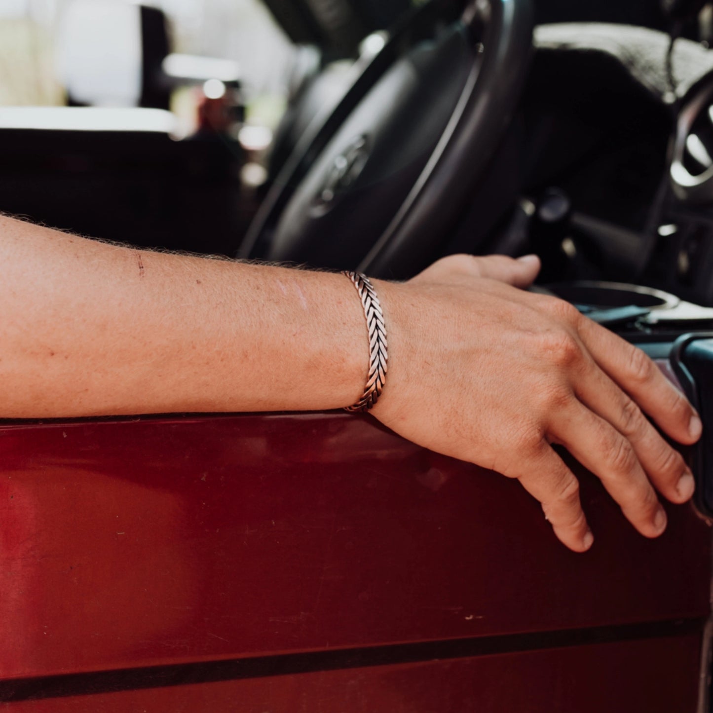 Hand wearing braided copper band resting on car door.