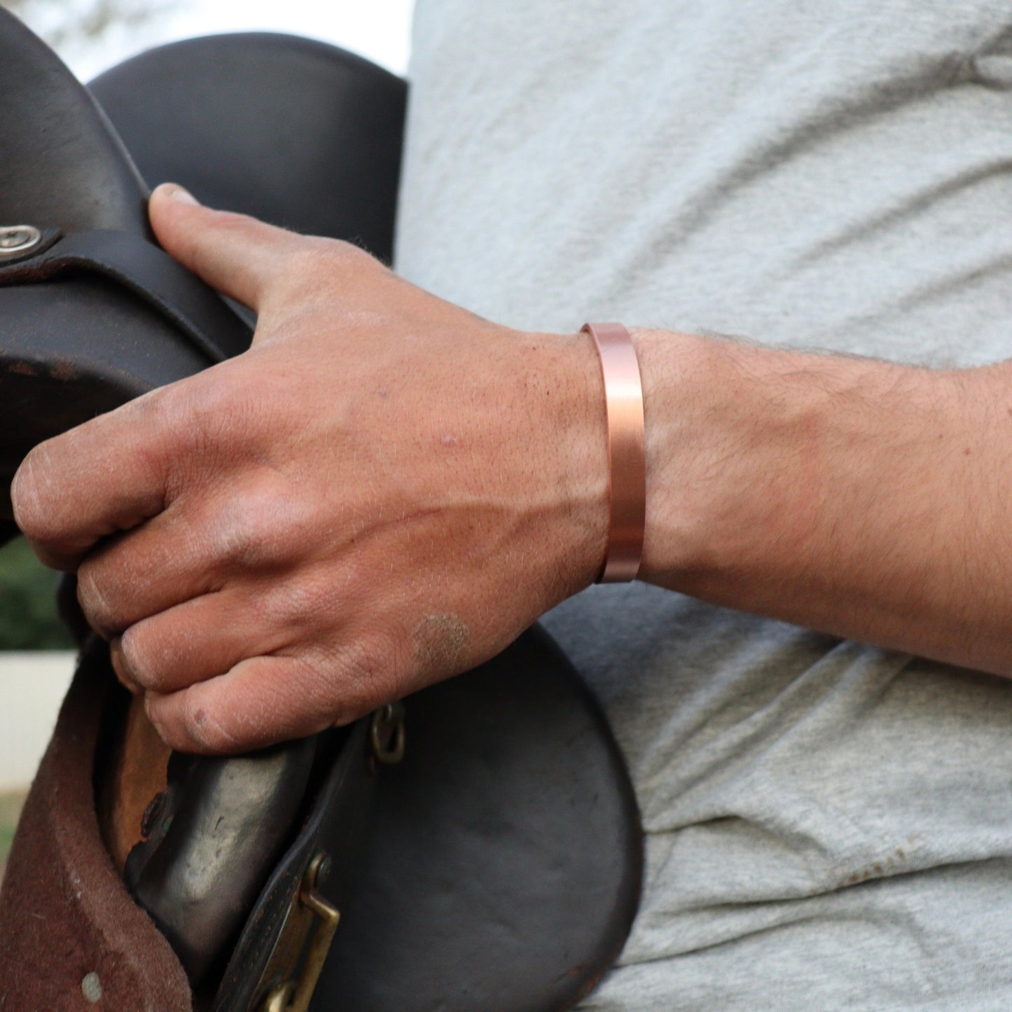 Hand holding a leather saddle with a copper bracelet on a blurred background