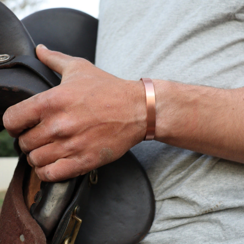 Hand holding a leather saddle with a copper bracelet on a blurred background
