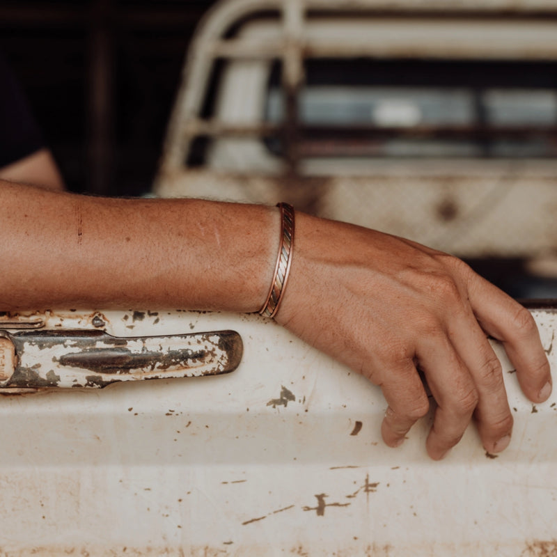 Hand wearing a tri-colour copper band on a rusted metal ute tray.