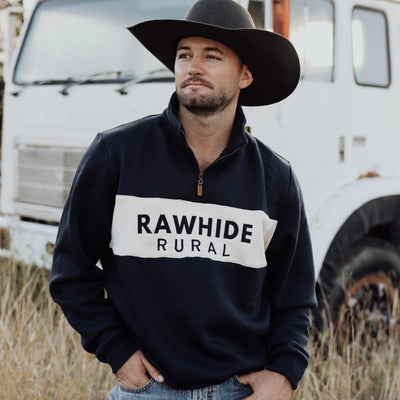 Man wearing a navy 'Rawhide Rural' sweatshirt with a grey hat in front of a white truck.