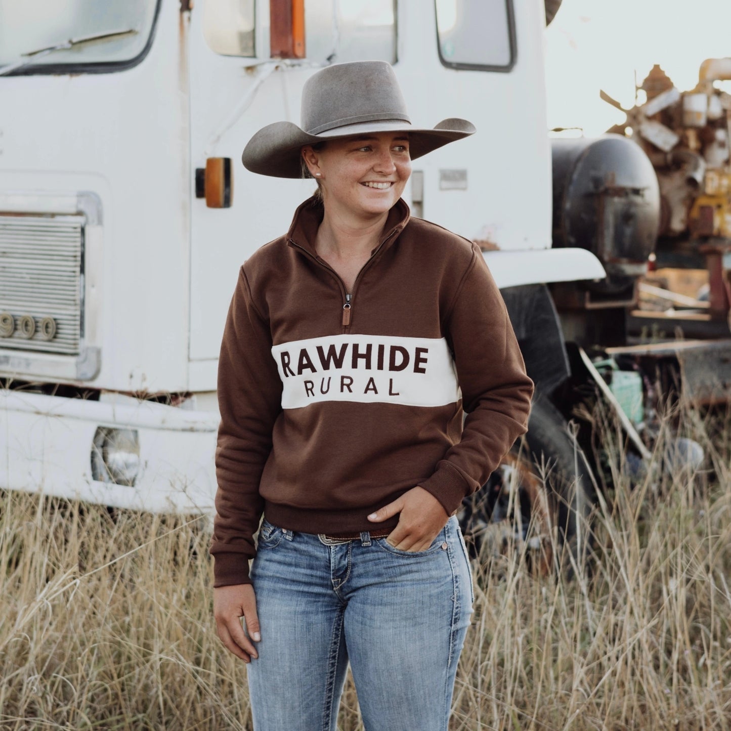 Person wearing a brown 'Rawhide Rural' jumper standing in front of a vintage truck.