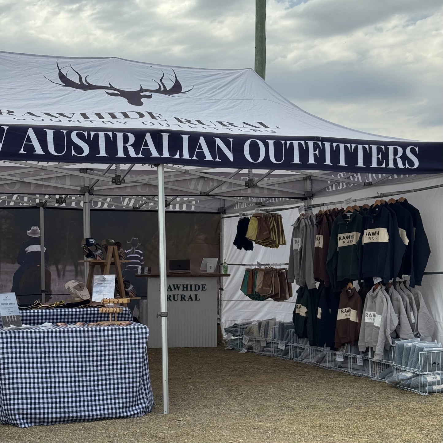 Outdoor stall with 'Australian Outfitters' branding displaying clothing and merchandise.