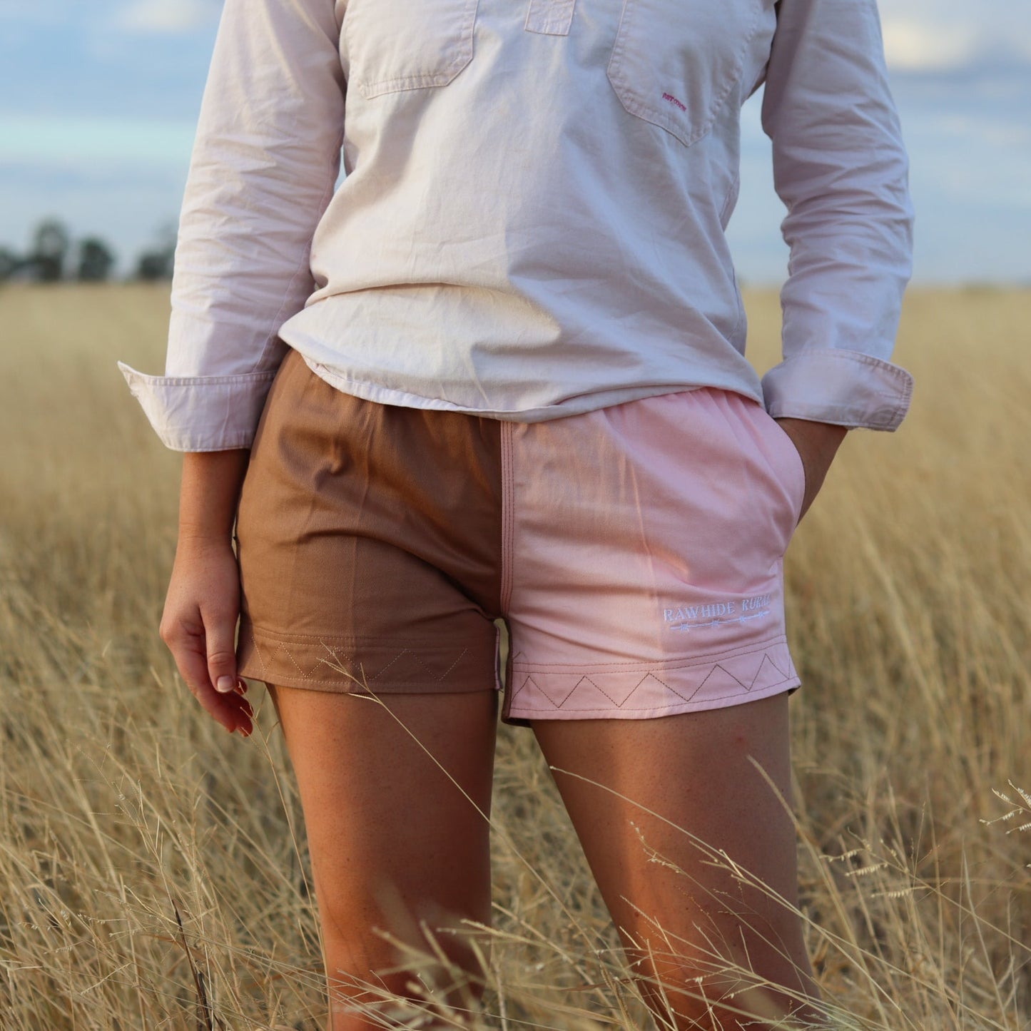 Person wearing a white shirt and brown shorts standing in a field with a blurred background